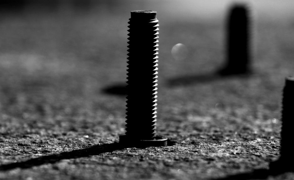 A detailed black and white close-up of a bolt standing upright on a textured surface.